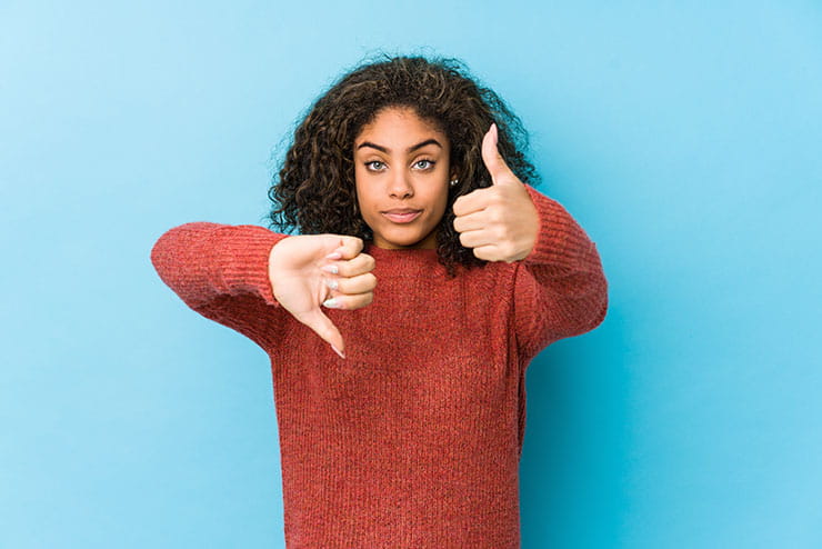 A young African American woman showing thumbs up and thumbs down, evaluating a decision. 