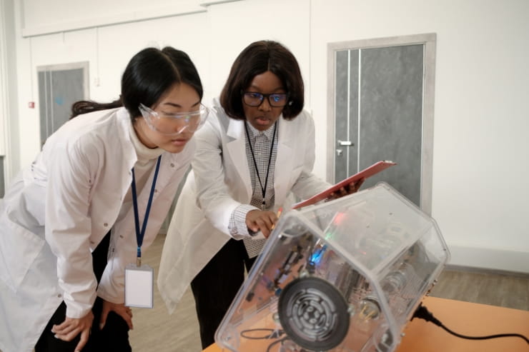 Female software engineer and scientist test electrical machinery in a robotics lab.
