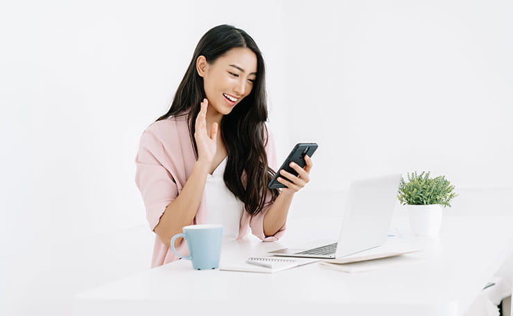 Woman sitting at desk waving hello to mobile phone